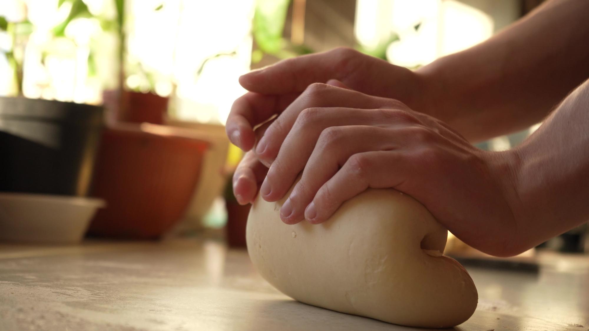 Hands kneading dough on wooden board
